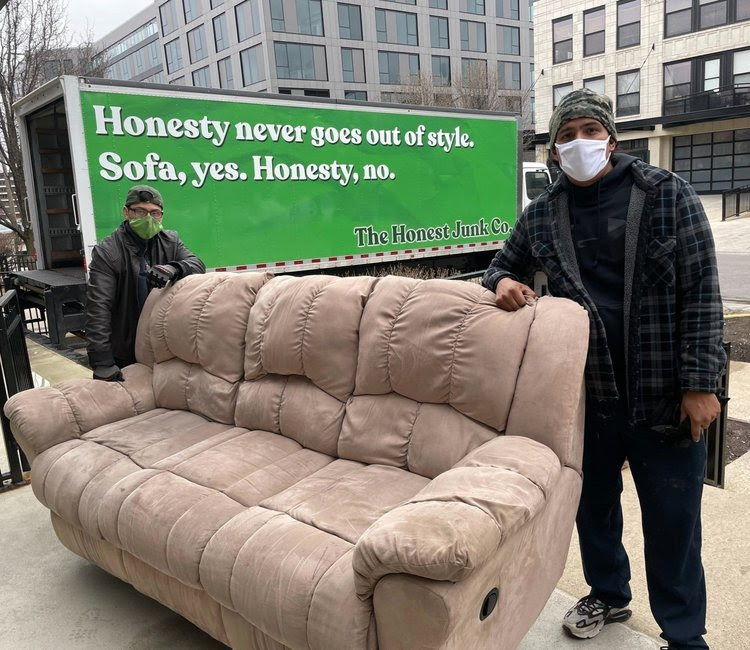 Two men with safety masks moving and old donated sofa into a green truck for junk removal as they donate.