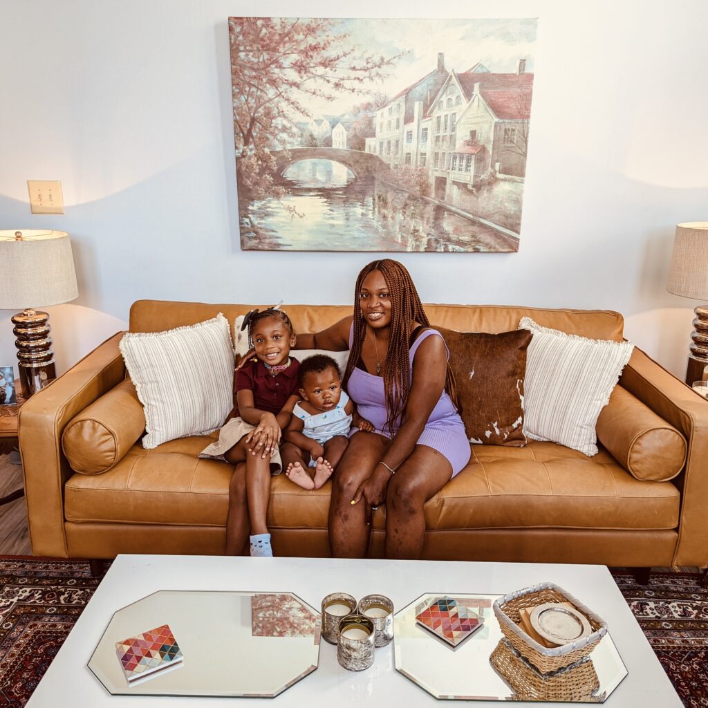 A mother and two young children sitting on a brown couch in their newly decorated living room.
